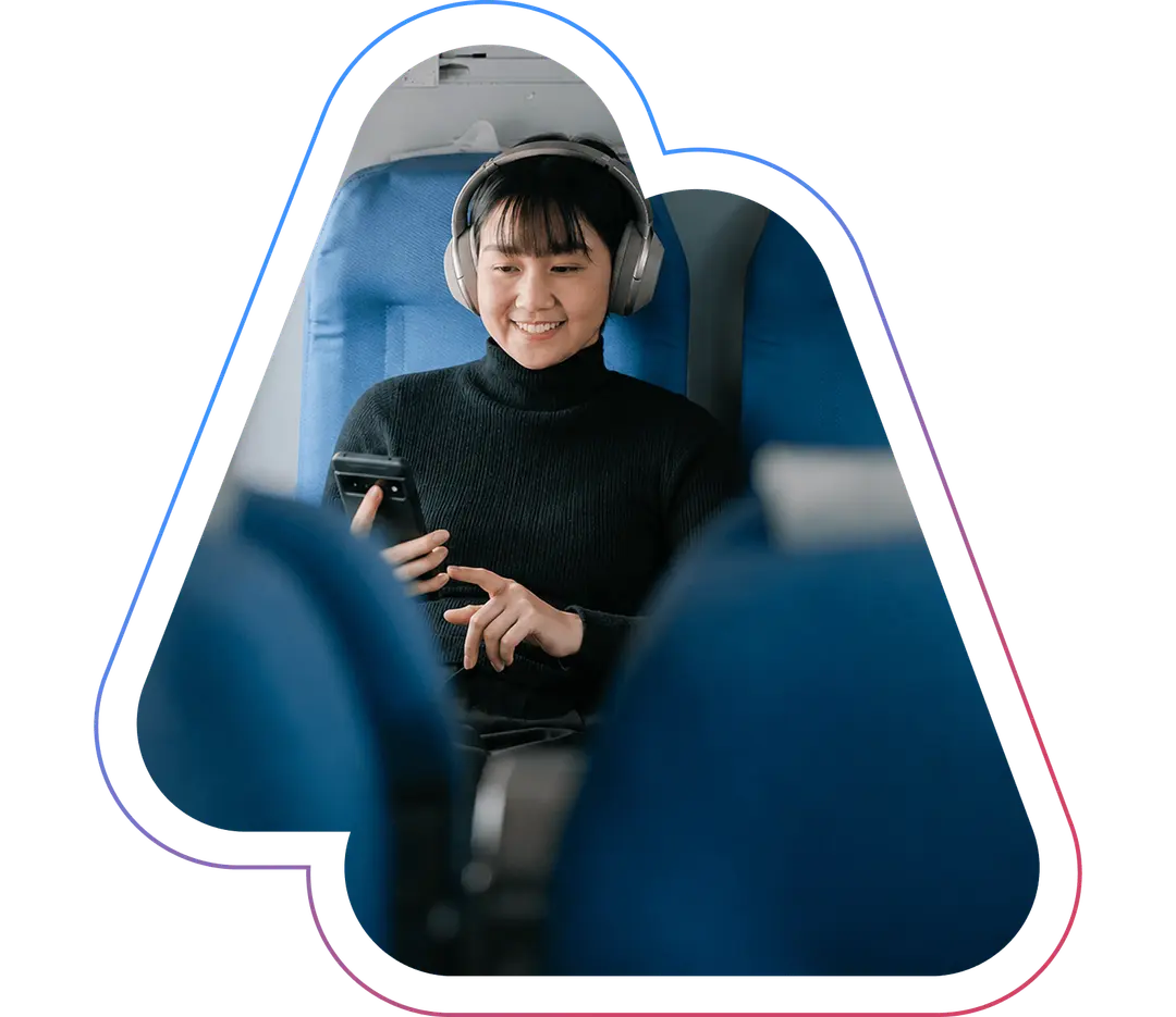 Person wearing headphones, smiling while using a smartphone, seated in a blue train seat.